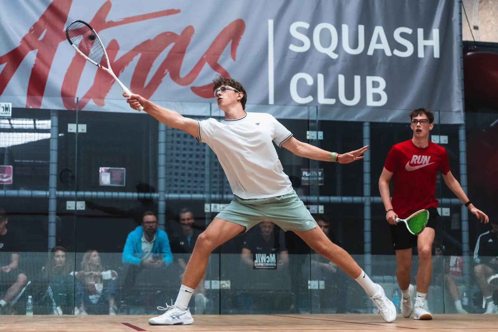 Mecz juniorów na szklanym korcie turniejowym pod banerem Atras Squash Club