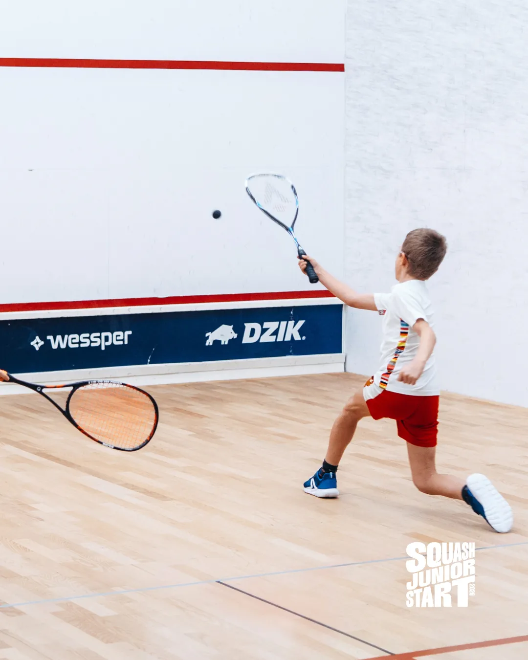 Chłopiec odbija piłkę podczas meczu squasha na korcie Atras Squash Club